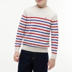 Model wearing cream cable-knit jumper with red and blue horizontal stripes and small Tommy Hilfiger flag logo, styled with dark jeans