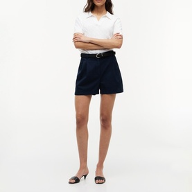 Model wearing navy tailored shorts with belt, styled with white polo shirt and black heeled mule sandals