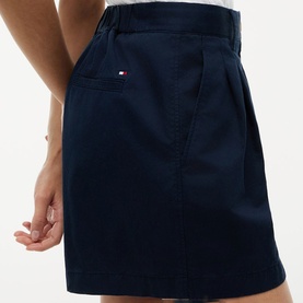 Model wearing Tommy Hilfiger navy blue pleated mini skirt with embroidered flag logo, shown from waist to mid-thigh, rear view.