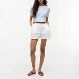 Model wearing white tailored shorts with a light blue ribbed top, brown leather belt, and tan flat sandals.