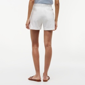 Model wearing white tailored shorts with turn-up hem, styled with tan flat sandals, back view