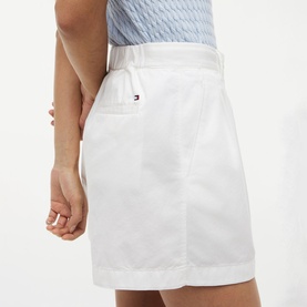 Model wearing white Tommy Hilfiger mini skirt with belt loops and back pocket, styled with a light blue top.