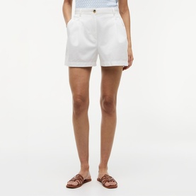 Model wearing white tailored shorts with pleat detail, styled with tan leather sandals
