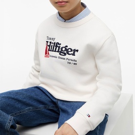 Model wearing white Tommy Hilfiger graphic crew neck sweatshirt with navy logo print, styled with blue denim jeans and striped collar shirt