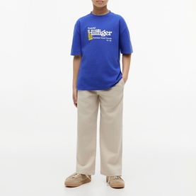 Model wearing Tommy Hilfiger Noble Blue graphic T-shirt, styled with beige wide-leg trousers and tan trainers
