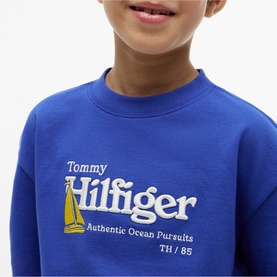 Model wearing Tommy Hilfiger Noble Blue sweatshirt with Authentic Ocean Pursuits graphic and sailboat embroidery detail.