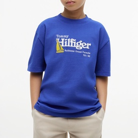 Model wearing Tommy Hilfiger Noble Blue graphic logo T-shirt, styled with beige trousers