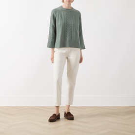 Model wearing Elena Miro flint green cable-knit wool jumper with three-quarter sleeves, styled with white cropped trousers and brown loafers.