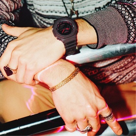 Model with Casio watch in brown, black and red, styled with gold chain bracelet and rings on model's wrists