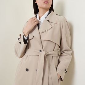 Model wearing HIGH Smuggler Trench Coat in beige, double-breasted with notch lapel, shoulder epaulettes, and matching belt. White shirt visible