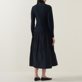 Model wearing HIGH Habit Shirt Dress in navy, rear view, showing raised shirt hem, gathered midi skirt, long sleeves, and one-button cuffs