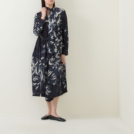 Model wearing HIGH Skive Printed Tie-Front Dress in blue abstract print, midi length with asymmetric hem, styled with black flat shoes.