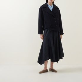 Model wearing HIGH Off Key Jacket in navy, single-breasted with notch lapel and epaulettes, styled with asymmetric skirt and taupe loafers