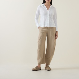 Model wearing HIGH Behave Slim Shirt in white with V-neckline and flared hem, styled with beige wide-leg trousers and loafers.