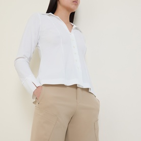 Model wearing HIGH Behave Slim Shirt in white with folded collar, V-neckline and pearl buttons, styled with beige tailored trousers