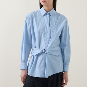 Model wearing HIGH Playful Tie Front Oversized Shirt in light blue cotton with wrap-style front, metal ring belt detail and pleated waist.