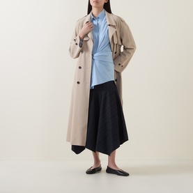 Model wearing HIGH Playful Tie Front Oversized Shirt in light blue, styled with a beige trench coat, black asymmetric skirt and black flats.