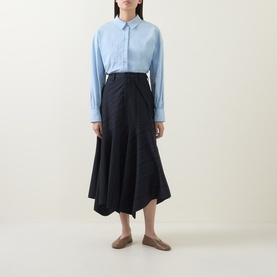 Model wearing HIGH Helix Asymmetric Pinstripe Skirt in navy, midi length with asymmetric hem, styled with light blue shirt and tan flats
