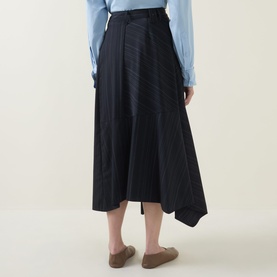 Model wearing HIGH Helix Asymmetric Pinstripe Skirt in navy, midi length with asymmetric hem, styled with a light blue shirt and tan loafers.