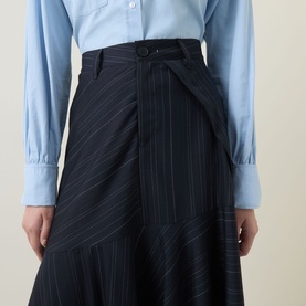 Model wearing HIGH Helix Asymmetric Pinstripe Skirt in navy, midi length with asymmetric hem, styled with a light blue shirt.