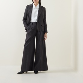 Model wearing HIGH Doff Pleated Pinstripe Trousers in dark grey with wide leg, styled with matching blazer and white shirt.