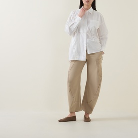 Model wearing HIGH Greece Barrell Leg Boyfriend Fit Trousers in beige, styled with a white oversized shirt and taupe flat shoes.