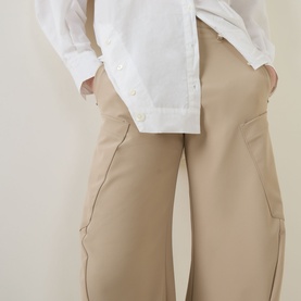 Model wearing HIGH Greece Barrell Leg Boyfriend Fit Trousers in beige with oversized side pocket detail, styled with a white shirt.