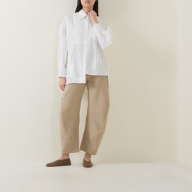 Model wearing HIGH Greece Barrell Leg Boyfriend Fit Trousers in beige with white oversized shirt and brown loafers.