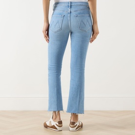 Model wearing Mother Crop Boot jeans in Room Service light blue denim, cropped flare leg with frayed hem, back view, styled with white trainers