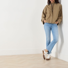Model wearing Mother Crop Boot jeans in Room Service light blue denim, styled with a beige zip-up jacket and white trainers.