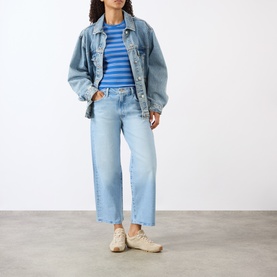 Model wearing Mother The Dodger Ankle Straight Jeans in Fringe Benefits light wash, styled with denim jacket, blue stripe top and beige trainers.