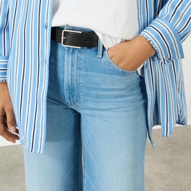 Model wearing Mother The Hustler High-Rise Wide Leg Jeans in Room Service light blue denim, styled with a black belt and blue striped shirt.