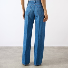 Model wearing Mother The Lasso Sneak Wide-Leg Jeans in mid-wash blue denim, wide-leg silhouette with pressed creases, rear view.