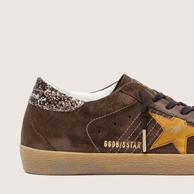 Golden Goose Super-Star brown suede trainer with mustard star, glitter heel tab, and gum sole, close-up detail shot