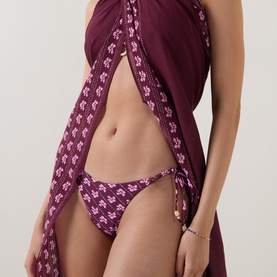 Model wearing Seafolly dark burgundy floral bikini brief with tie sides, styled with matching burgundy sarong wrap.