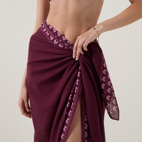 Model wearing Seafolly dark burgundy cotton sarong with floral embroidered trim, tied at hip, paired with matching bikini top