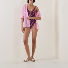 Model wearing Seafolly dark burgundy floral one-piece swimsuit, styled with pink oversized shirt and white slider sandals.