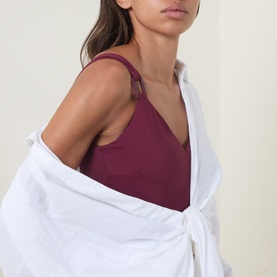 Model wearing Seafolly dark burgundy swimsuit with V-neckline, styled with a white shirt tied around the waist.