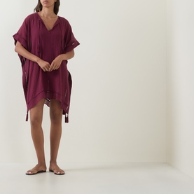 Model wearing Seafolly dark burgundy cotton kaftan cover-up with V-neck, short sleeves, tassel ties, and drawstring hem, styled with flat sandals