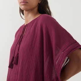 Model wearing Seafolly dark burgundy cotton cover-up with tassel tie neckline, ladder trim detailing on sleeves, and relaxed kaftan silhouette