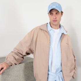 Model with Acne cornflower blue cotton cap, styled with a beige zip-up jacket and light blue striped shirt.