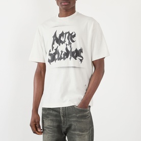Model wearing Acne Gothic Logo T-Shirt in dusty white with gothic spray-painted logo print, styled with distressed grey jeans.