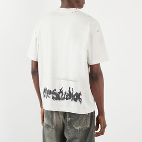 Model wearing Acne Gothic Logo T-Shirt in dusty white, rear view showing gothic spray-painted logo, distressed detail, styled with blue wash jeans.