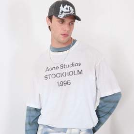 Model with Acne Gothic Logo Baseball Cap in faded black, peak visor, spray-painted logo, styled with white Acne Studios graphic tee
