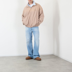 Model wearing Acne Washed Logo Jacket in Mushroom Beige with light blue wide-leg jeans and brown suede shoes.