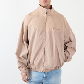 Model wearing Acne Washed Logo Jacket in mushroom beige, high collar, zip fastening, styled with light blue jeans.