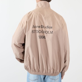 Model wearing Acne Washed Logo Jacket in mushroom beige, rear view showing logo stamp print, high collar and elasticated hem.