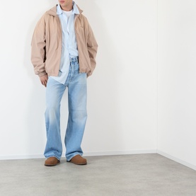 Model wearing Acne Washed Logo Jacket in Mushroom Beige with light blue shirt, wide-leg light wash jeans and tan suede loafers