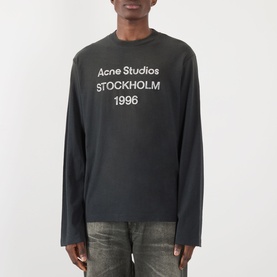 Model wearing Acne Sprayed 1996 Logo T-Shirt in faded black, long-sleeve crew neck with Stockholm 1996 stamp logo print, styled with distressed jeans