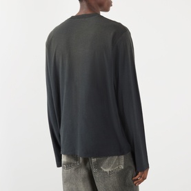 Model wearing Acne Sprayed 1996 Logo T-Shirt in faded black, long-sleeve crew neck with dropped shoulders, styled with grey distressed jeans.